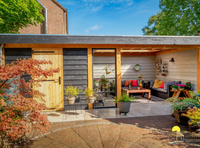 Veranda met kleine berging in de tuin met veel kleurrijke bloemen en planten