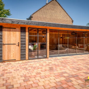 Grote veranda met kleine berging met rode tegels in de tuin en grote glazen schuifwand en ramen